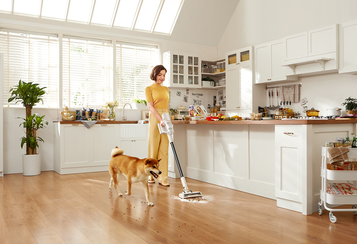 Απεικονίζεται μια γυναίκα να καθαρίζει στην κουζίνα και δίπλα της ένας σκύλος.